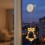 A small holiday window light with a clear suction cup mount and a glowing bell-shaped bulb hanging in front of a window at dusk.
