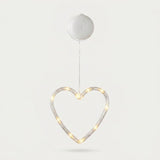 Clear heart-shaped window light glows warm white beneath a round white battery box against a pale background.