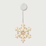 A clear snowflake-shaped window light glows with warm LEDs beneath a round white housing against an off-white background.