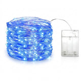 Blue LED fairy string lights coiled in a ball next to a clear plastic battery compartment on a white background.