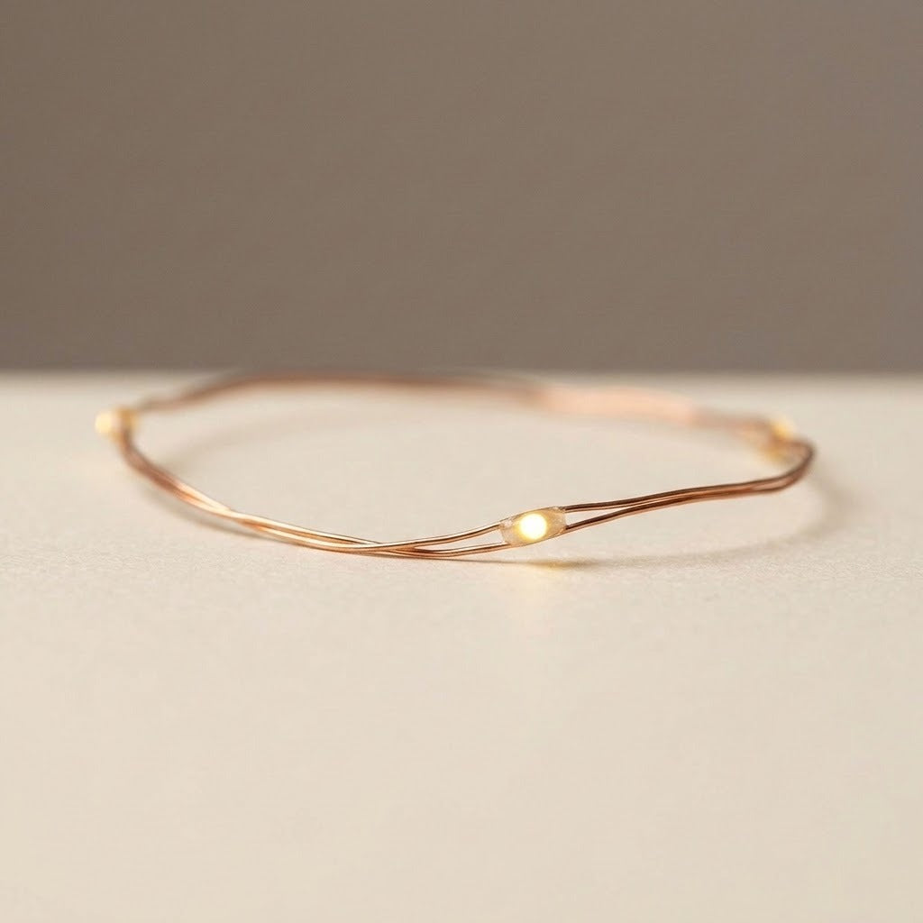 Copper wire string lights form a loose loop on a pale beige surface, with a glowing warm white LED in close-up.