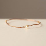 Copper wire string lights form a loose loop on a pale beige surface, with a glowing warm white LED in close-up.