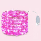 Pink LED fairy string lights coiled in a roll with a visible USB connector cable on a solid pale pink background.