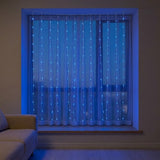 Blue curtain string lights hanging in front of a window in a dimly lit room, casting a cool blue glow on the curtains and surrounding wall.