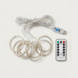 An unlit LED curtain light has coiled clear strands, a USB controller with a blue button, and a white remote on light gray.