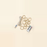 An unlit LED curtain light lies diagonally on a beige background with coiled clear strands, a USB controller, and a white remote.