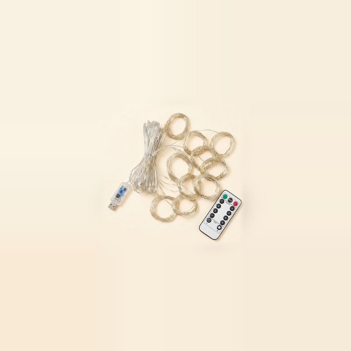 An unlit LED curtain light lies diagonally on a beige background with coiled clear strands, a USB controller, and a white remote.
