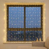 Warm white curtain string lights draped over a dark-framed window at dusk, with a beige sofa partially visible in the foreground.