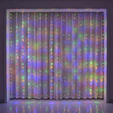 Multicolor LED curtain string lights hanging vertically in front of sheer white curtains, casting a soft rainbow of light onto a dark wall and floor.
