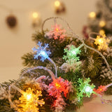 Multicolor LED snowflake string lights glowing on a decorated Christmas tree, with green, blue, red, and yellow snowflake-shaped bulbs among frosted pine branches.