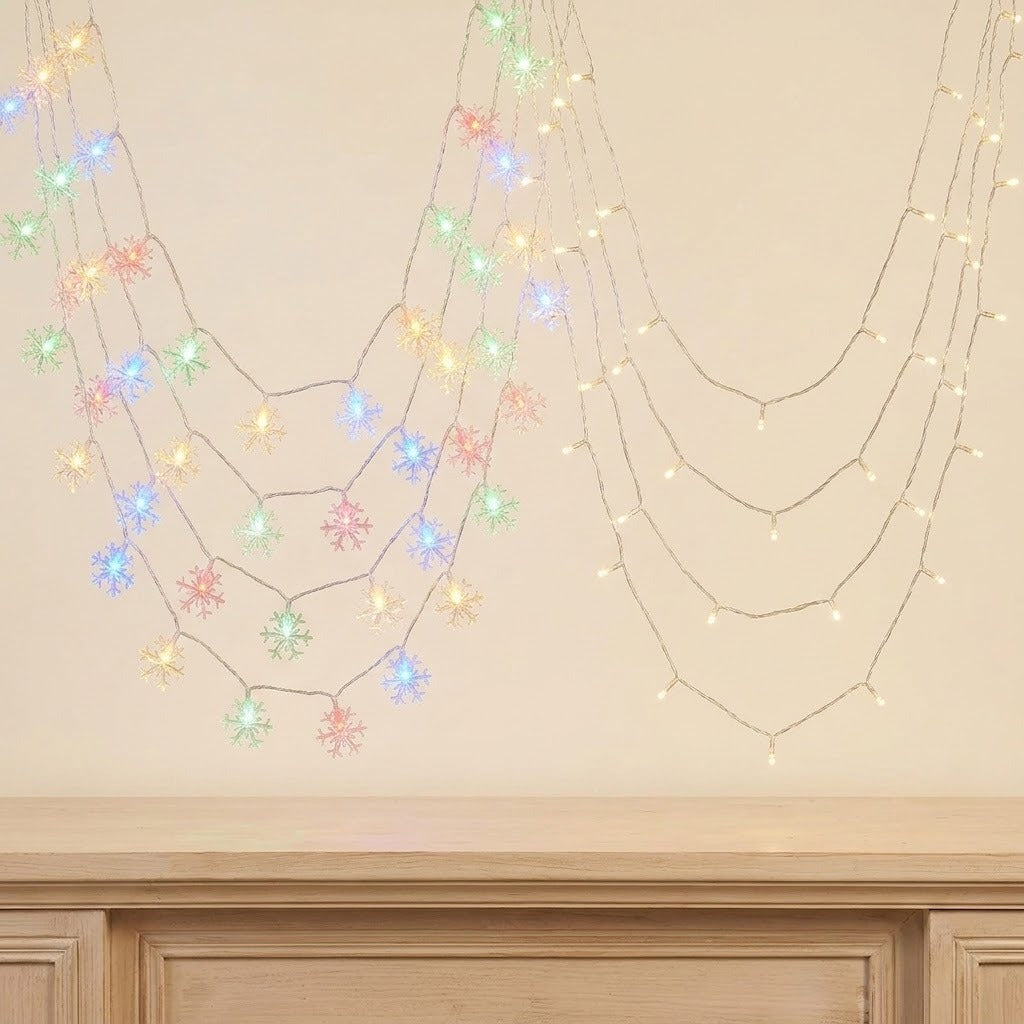 Multicolor snowflake LED fairy string lights draped in two curved rows against a beige wall above a wooden mantel.