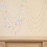 Multicolor snowflake LED fairy string lights draped in two curved rows against a beige wall above a wooden mantel.