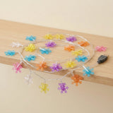 Multicolor snowflake-shaped LED fairy string lights coiled on a light wood shelf, with a black USB plug visible on the right side.