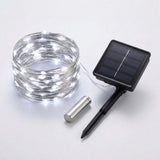 Solar string lights with a coiled wire of glowing white LED bulbs, a small rectangular solar panel stake, and a silver metal battery, shown on a light gray background.