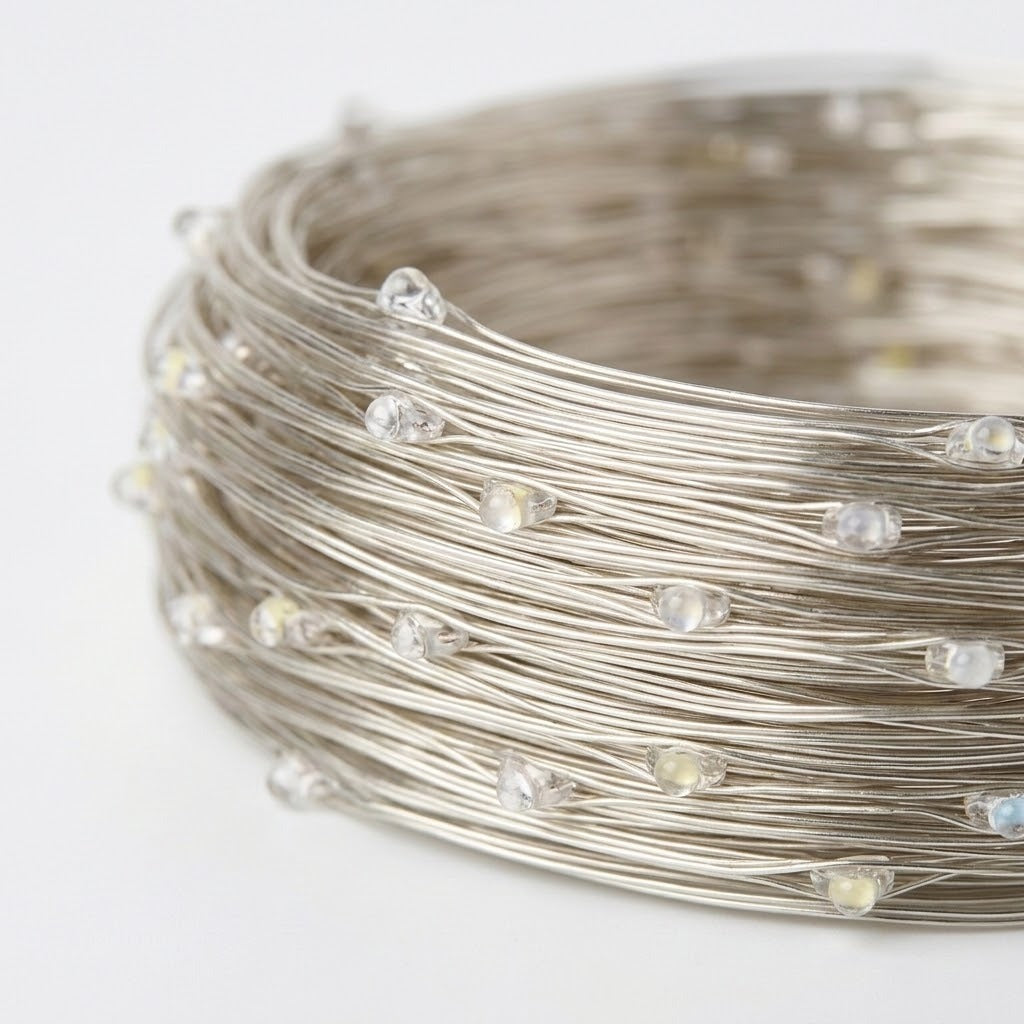 A close-up of a coiled bundle of silver-colored wire string lights with small clear faceted bulbs on a plain white background.
