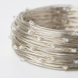 A close-up of a coiled bundle of silver-colored wire string lights with small clear faceted bulbs on a plain white background.