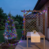 Multicolor LED garden string lights draped over a wooden lattice patio trellis and a decorated Christmas tree at dusk.
