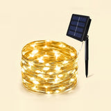 Coiled solar string lights glowing warm white, with a small black solar panel and stake attached, shown on a plain light beige background.