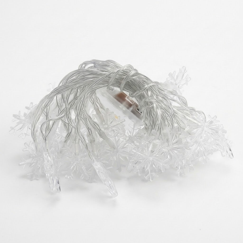 Unlit snowflake curtain lights with clear wire lie coiled on a white background.