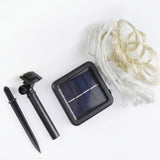 Solar LED curtain light with coiled clear wiring, a black solar panel, and separate ground stake components on a white background.