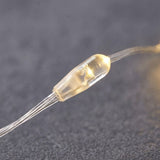 Close-up of a curtain light’s warm white LED inside a clear plastic capsule, with transparent wiring against a dark textured background.