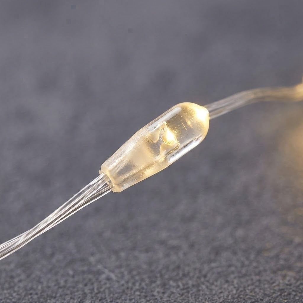 Close-up of a curtain light’s warm white LED inside a clear plastic capsule, with transparent wiring against a dark textured background.