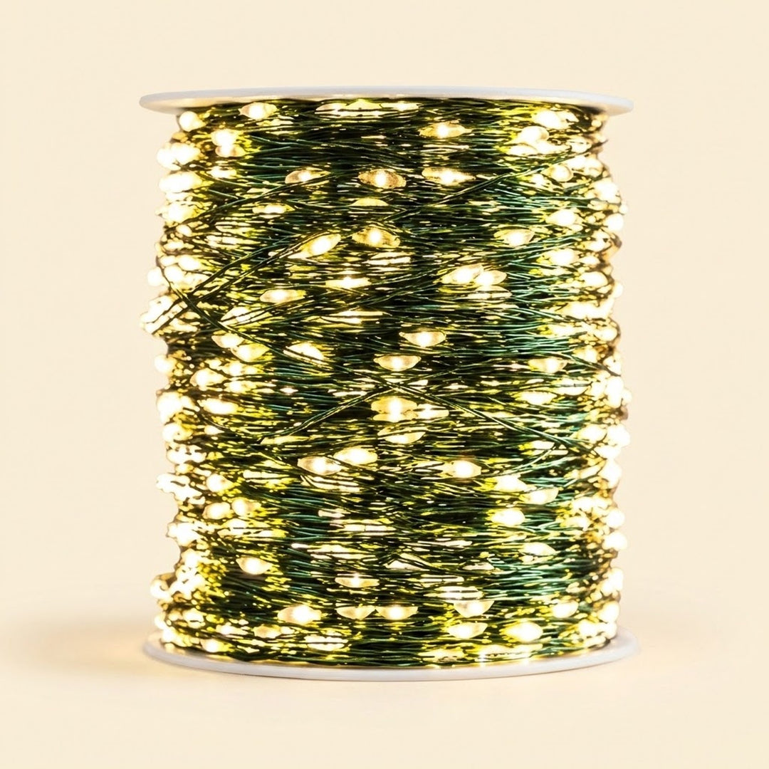 A spool of green wire Christmas string lights glowing with warm yellow lights, set against a solid light beige background.