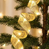 A gold mesh ribbon light string with star patterns and warm white lights spirals between green Christmas tree branches.