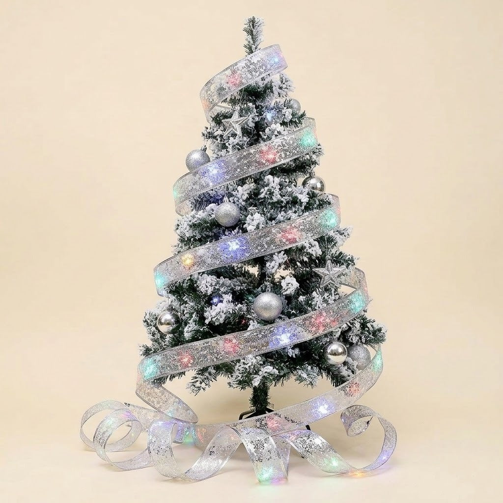 A silver ribbon light string with multicolored lights spirals around a flocked Christmas tree with silver ornaments against a beige background.
