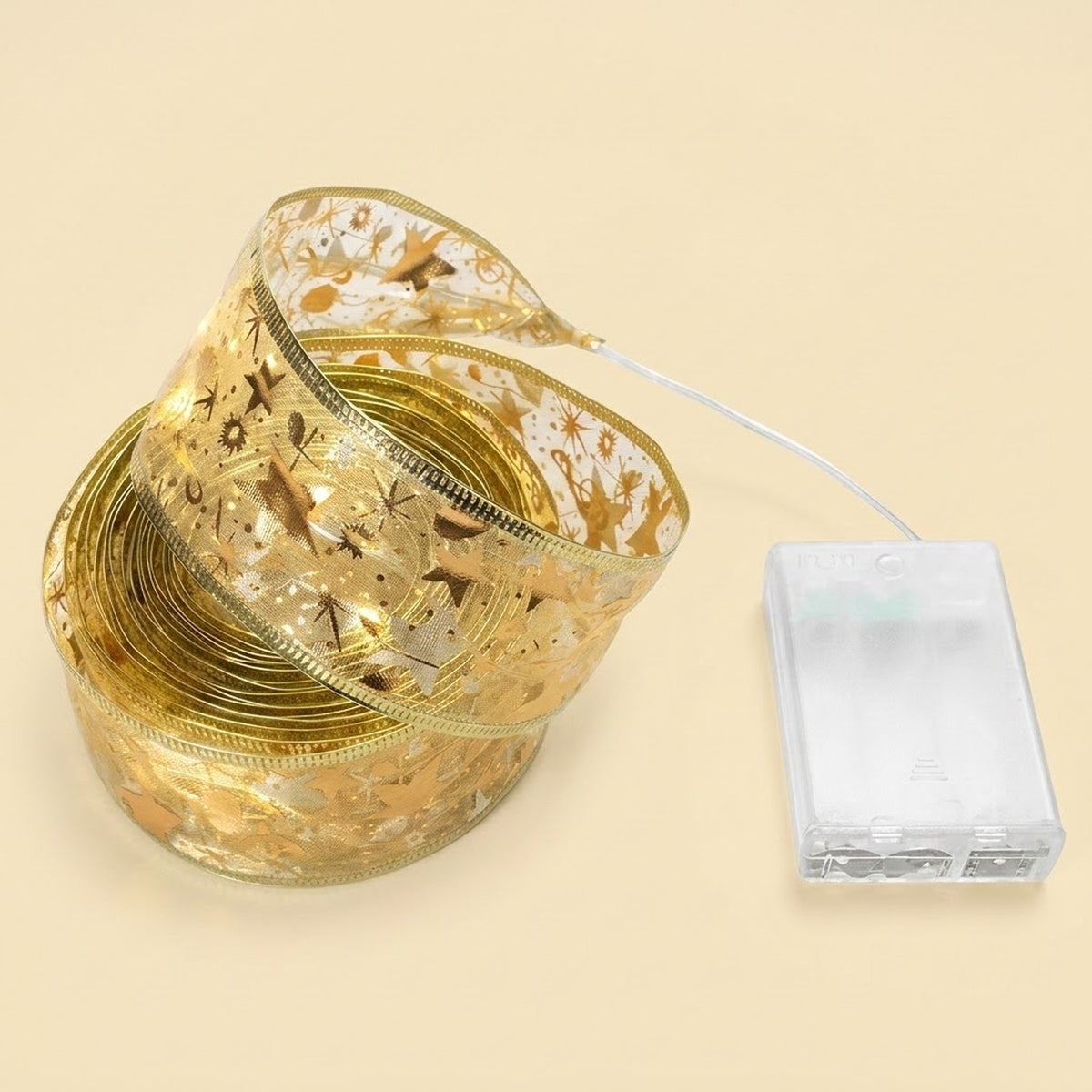 Sheer gold ribbon light string with festive patterns sits coiled beside a clear battery box on a pale yellow background.