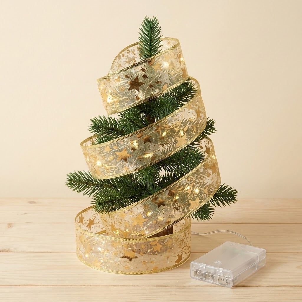 A gold ribbon light string wraps around a small Christmas tree, with its connected clear battery box resting on the wooden tabletop.