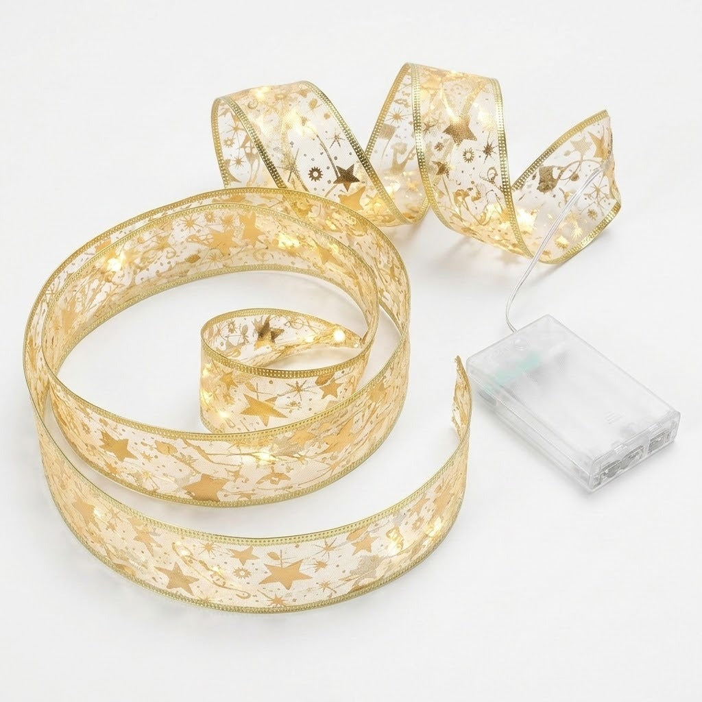 A gold ribbon light string with star and snowflake patterns glows warmly beside a clear battery pack on a white background.