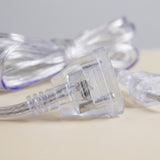 A transparent extension cord’s clear plastic female connector rests on a beige surface, with the bundled cable blurred behind.
