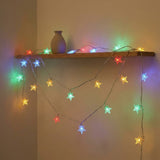 Multicolor star-shaped LED string lights draped over a wooden shelf with a small vase, casting colorful light on a beige wall.