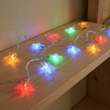 Multicolor star-shaped LED string lights draped across a light wood shelf, glowing in red, orange, yellow, green, blue, and purple.