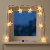Warm white star-shaped LED string lights arranged around a window frame on a shelf, with a USB cable visible at the bottom against a beige wall.