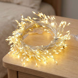 Warm white LED fairy string lights coiled on a light wood table in a bedroom setting.