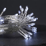 Close-up of a bundle of clear LED string lights on thin silver wires, with several bulbs illuminated, set against a dark background.