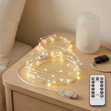 Coiled warm white LED fairy string lights on a wooden bedside table next to a white diffuser bottle, with a black inline switch and a white remote control.