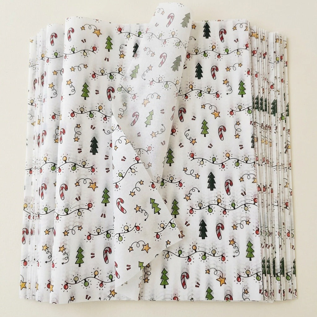White tissue wrapping paper sheets are stacked on a cream background, with one translucent corner lifted to reveal the Christmas pattern.