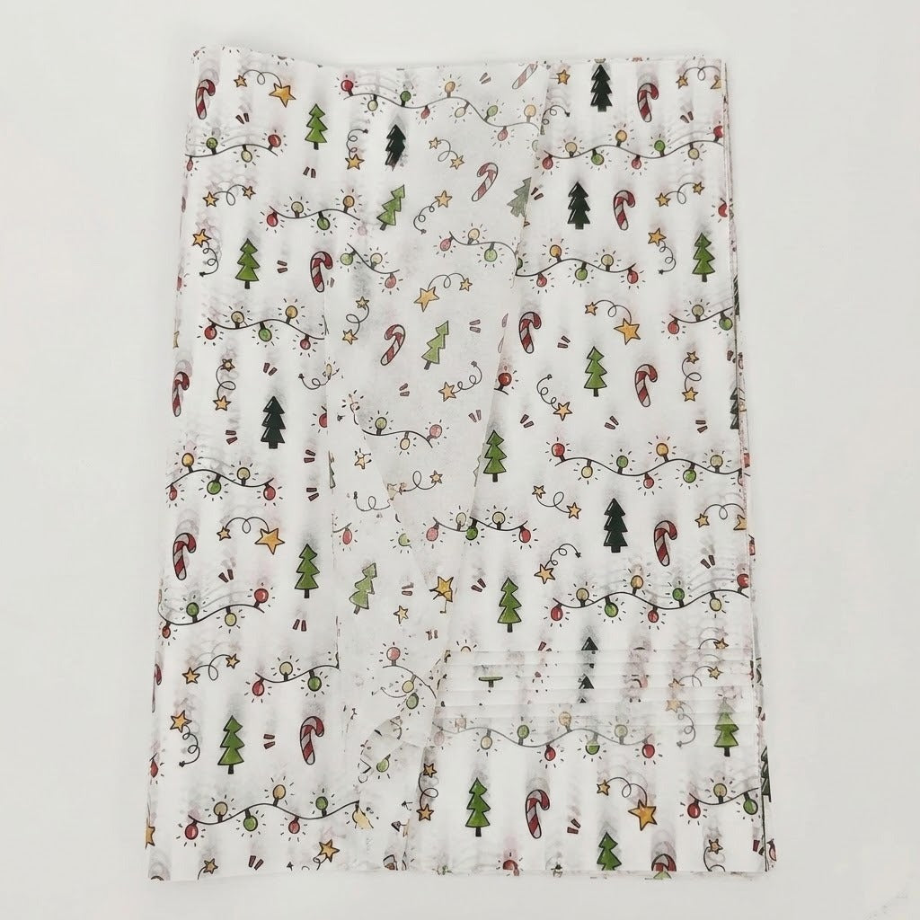 White tissue wrapping paper with green trees, red candy canes, and yellow stars lies in overlapping translucent layers on a pale background.