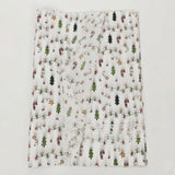 White tissue wrapping paper with green trees, red candy canes, and yellow stars lies in overlapping translucent layers on a pale background.