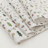 White tissue wrapping paper is loosely folded on a pale surface, showing green trees, red candy canes, yellow stars, and multicolored string lights.