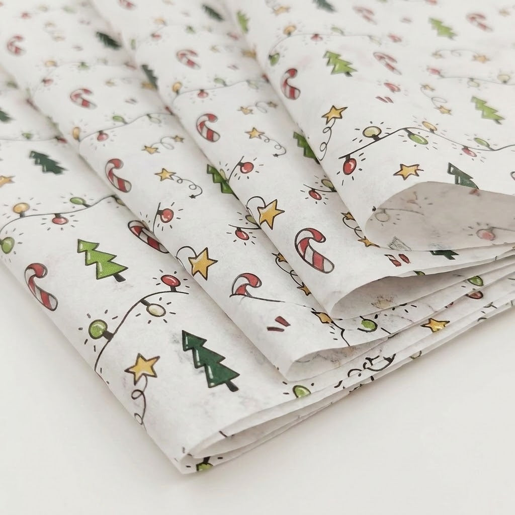 White tissue wrapping paper is loosely folded on a pale surface, showing green trees, red candy canes, yellow stars, and multicolored string lights.