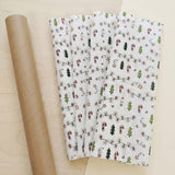 White wrapping paper with green trees, red candy canes, and yellow stars lies beside rolled brown paper on a pale wooden surface.
