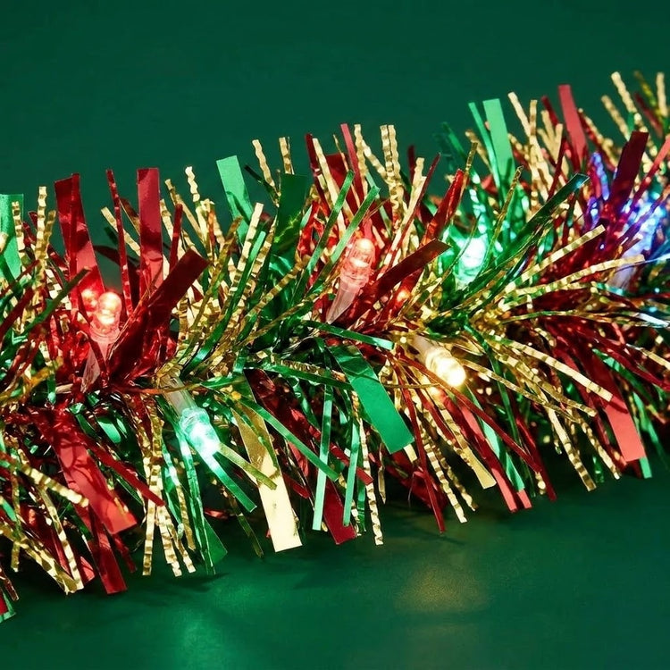 Red, green, and gold Christmas tinsel garland with built-in LED lights, photographed on a dark green background.