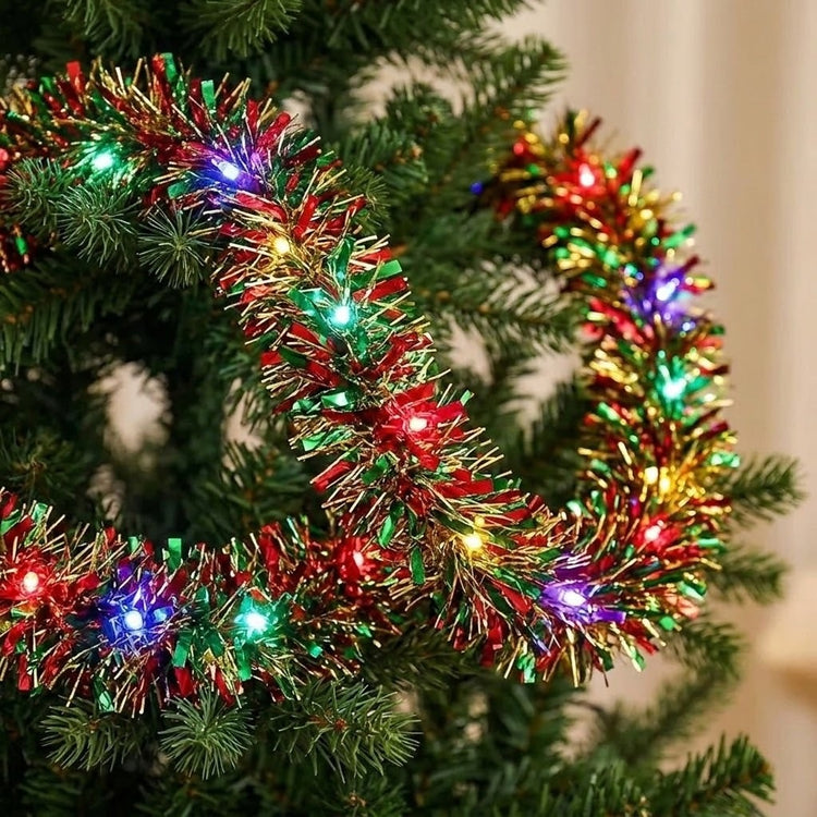 A red, green, and gold metallic tinsel Christmas garland with multicolor LED lights drapes across Christmas tree branches.