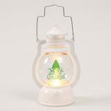 White decorative lantern with wire handle, warm light, green Christmas tree and Merry Christmas lettering against a pale background.