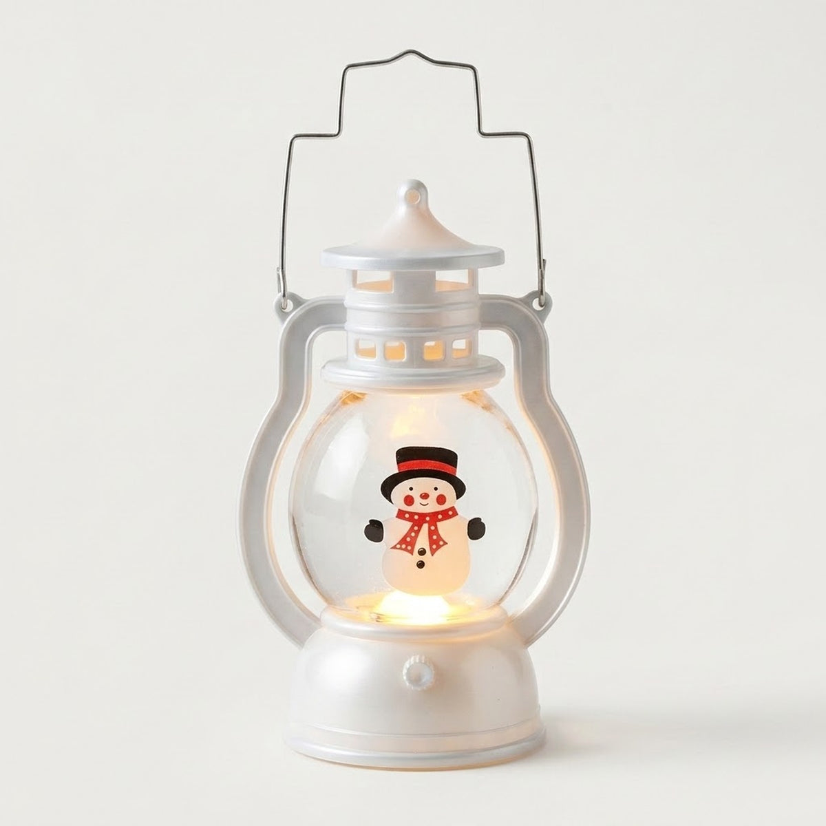 White decorative lantern with wire handle, warm light and snowman design featuring a black hat and red scarf against a pale background.