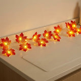 Warm white LED maple leaf string lights glowing on a white countertop against a beige wall.